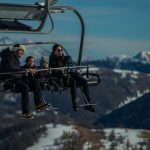 Family having fun on a ski lift with snow-covered mountains in the background during a sunny winter day.