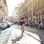 Energetic woman jogger running down a city street in active wear on a sunny day.